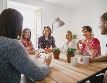 Group of employees at a small coffee shop sitting around a table having a meeting.